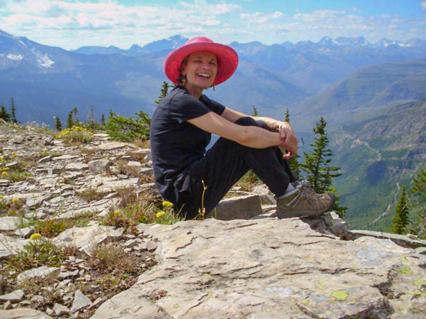 Photograph of Teresa Diffley sitting on cliff with forest and sky background.
