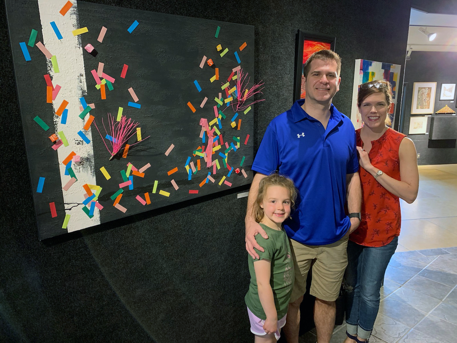 Photograph of After the Parade painting with man, woman, and female child posing for photograph nearby.